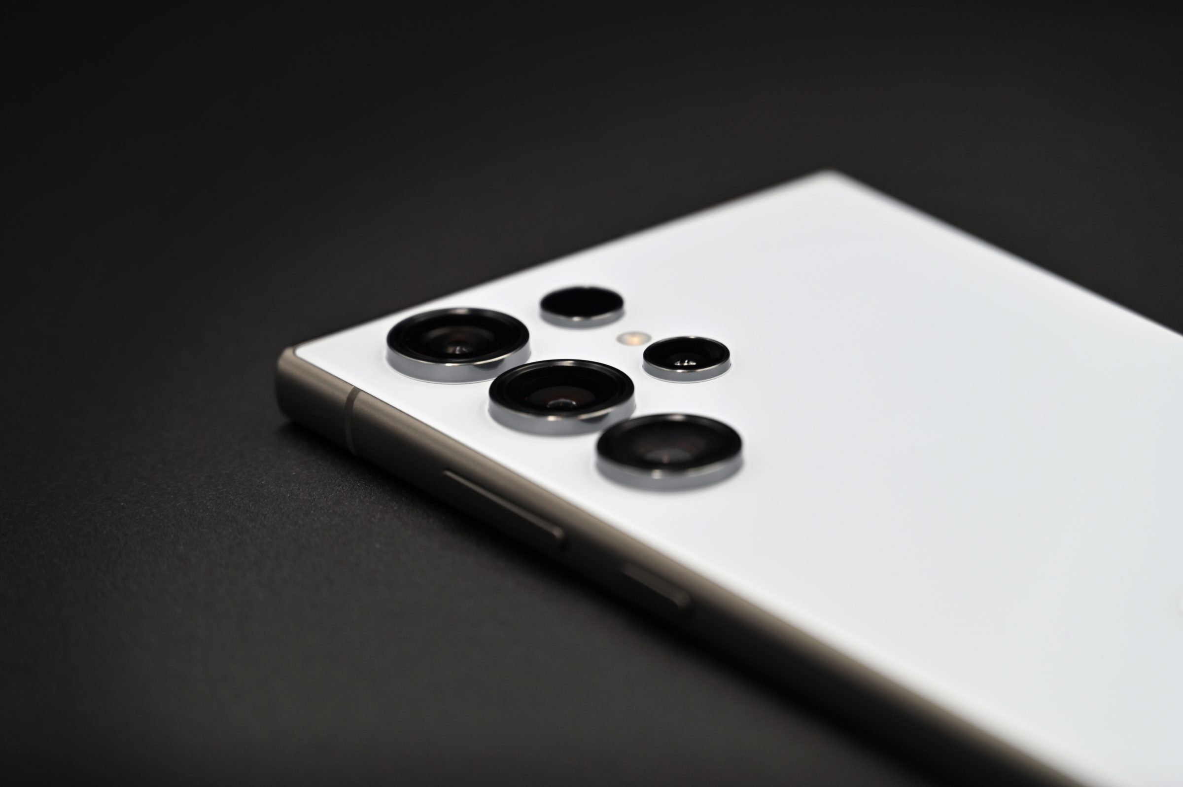 De achterkant van een witte Samsung Galaxy S24 Ultra met de camera's, op een donkere ondergrond